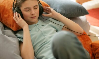 A young girl with closed eyes enjoys music through wired headphones while reclining indoors.