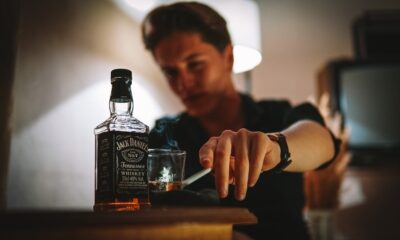 A moody image of a man smoking with a glass of whiskey indoors.