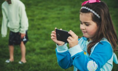 A young girl with a smartphone taking a photo in a grassy park setting