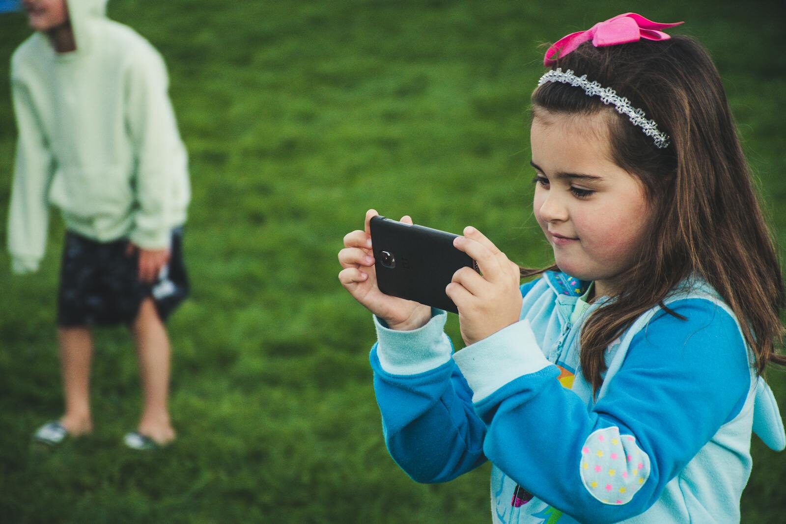 A young girl with a smartphone taking a photo in a grassy park setting