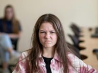An angry teenage girl sitting in a classroom, displaying a frustrated expression.