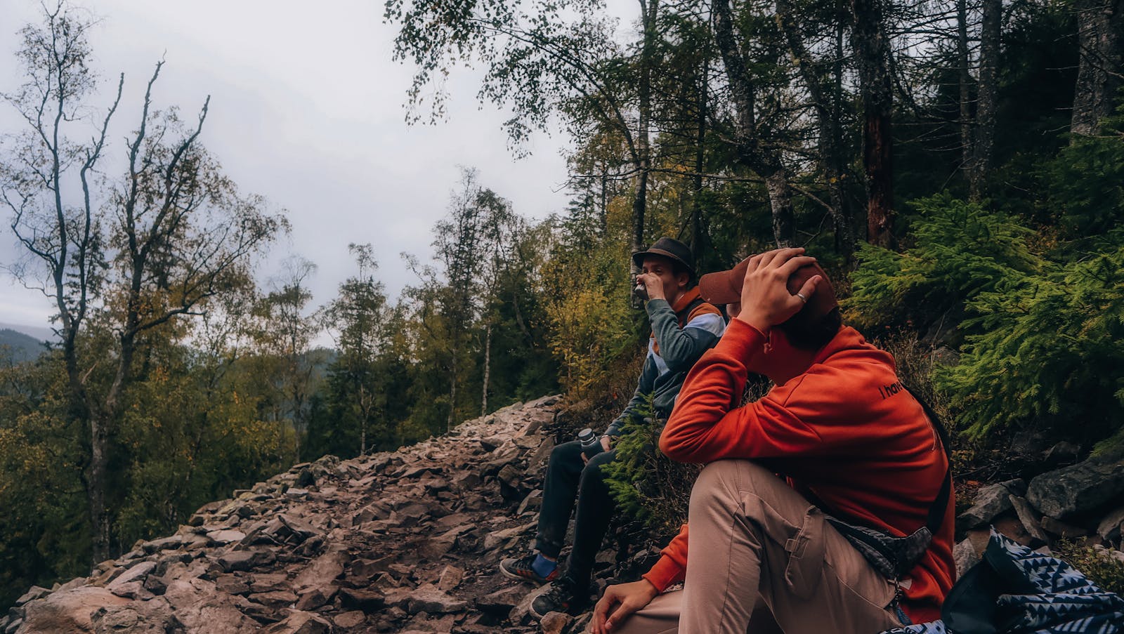 Two hikers in vibrant autumn forest pause along the rocky trail, capturing the beauty of nature.