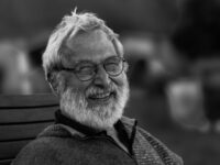 Black and white close-up portrait of a smiling elderly man with a beard and eyeglasses.