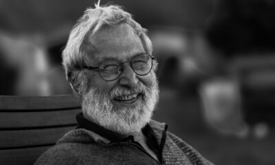 Black and white close-up portrait of a smiling elderly man with a beard and eyeglasses.