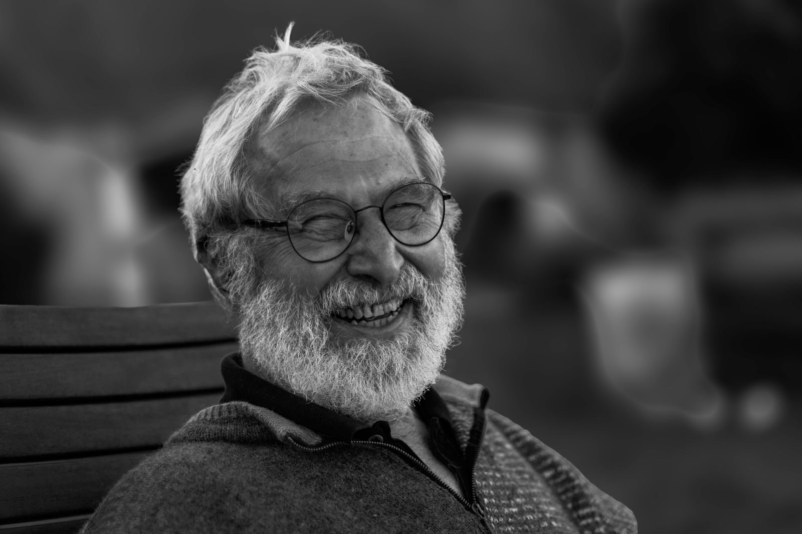 Black and white close-up portrait of a smiling elderly man with a beard and eyeglasses.