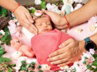 Sweet newborn wrapped in pink, nestled among floral decorations, symbolizing love and warmth.
