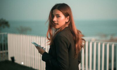 Stylish young woman holds smartphone with a scenic sea backdrop outdoors.
