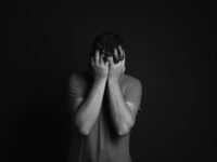 A grayscale portrait of a man covering his face, depicting emotion and mental health themes.