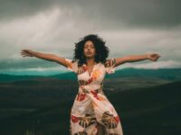 A woman in a flowing dress enjoys peaceful moments in a vast, cloudy landscape.