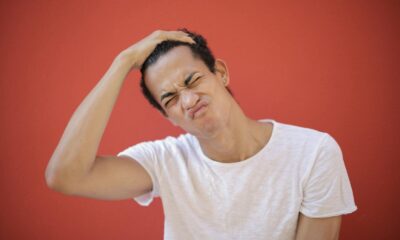 Happy ethnic with piercing putting hand on head and frowning face while standing against red background
