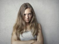 Portrait of a fierce woman with crossed arms and intense expression on a gray background.