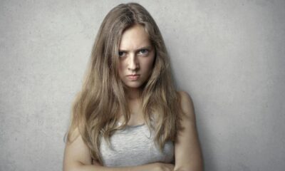 Portrait of a fierce woman with crossed arms and intense expression on a gray background.