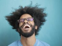 Portrait of a joyful man laughing with an afro hairstyle against a blue background.