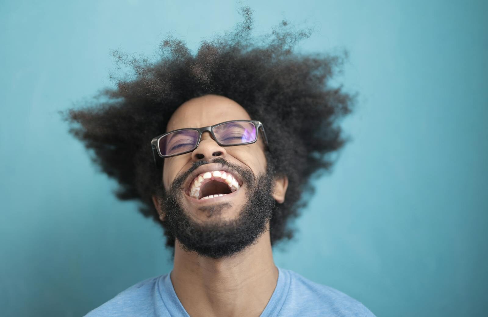 Portrait of a joyful man laughing with an afro hairstyle against a blue background.