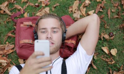 A young man lying on grass with headphones, enjoying music and using his smartphone in a park.