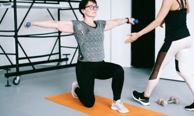 Two women working out with dumbbells on yoga mats in a modern gym setting, focusing on strength training.