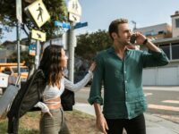 A couple has an intense discussion outdoors on a sunny street corner.