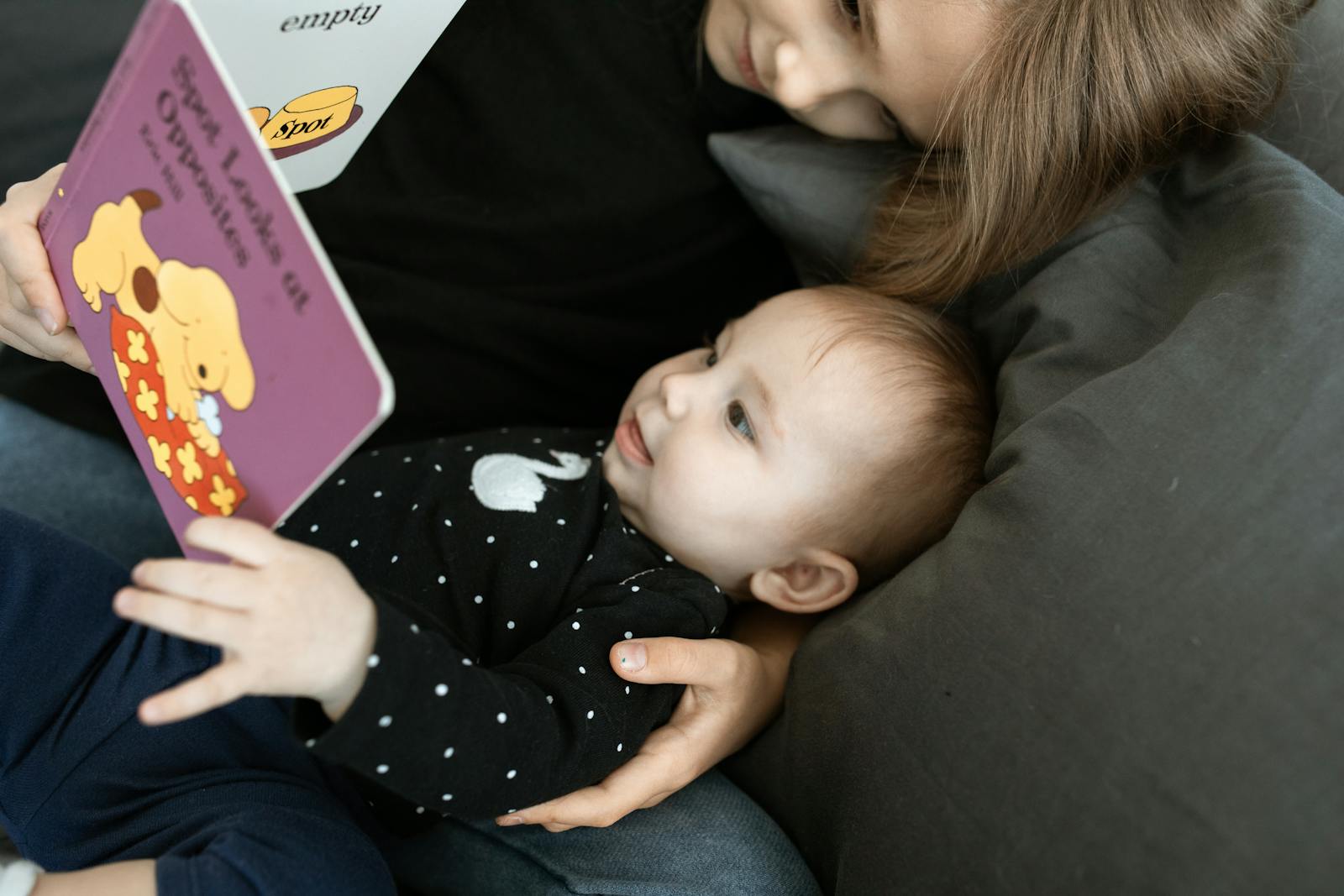 A touching scene of a big sister reading to her baby sibling on a cozy sofa.