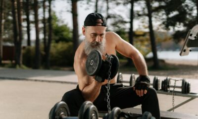 Elderly man lifting dumbbells in an outdoor gym setting, promoting healthy lifestyle.