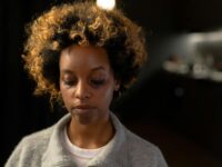 A woman with a bruise on her face, looking thoughtful in an indoor setting.