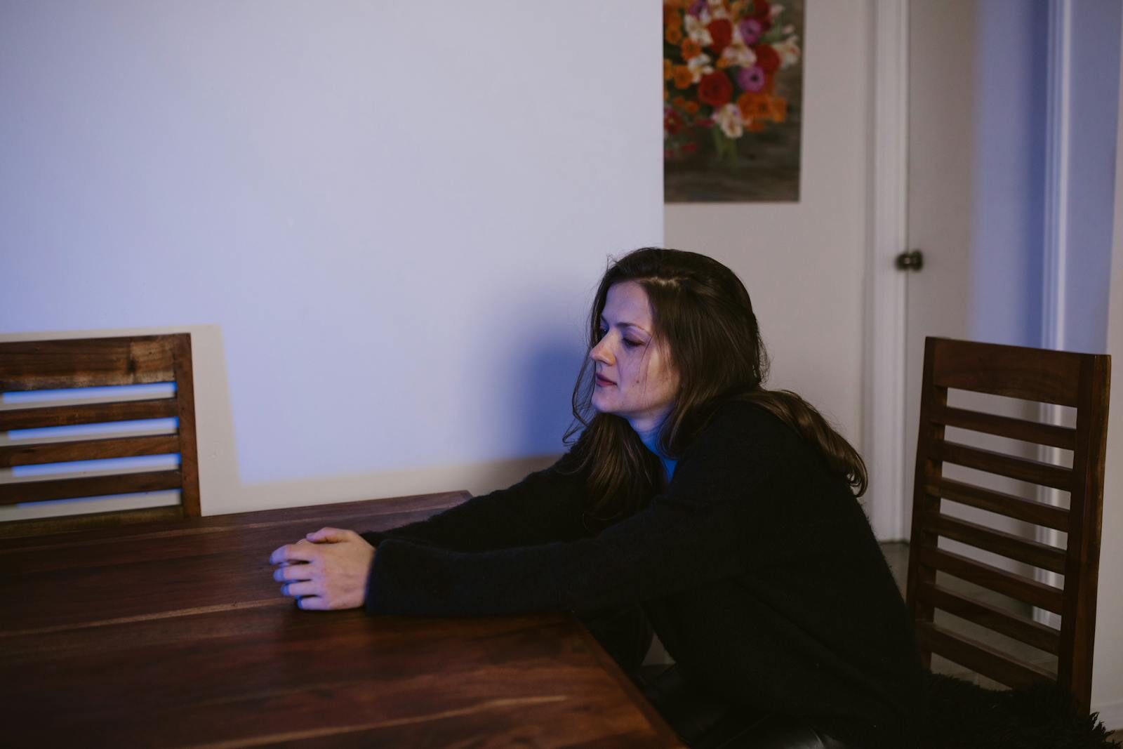 Woman sitting alone at a dining table, contemplating in a dimly lit room.