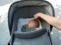 A serene moment of a baby sleeping in a stroller with a gentle touch from an adult hand.