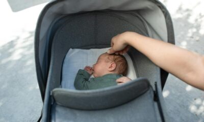 A serene moment of a baby sleeping in a stroller with a gentle touch from an adult hand.