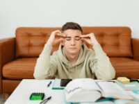 Young man experiencing stress while studying at home, wearing a hoodie.