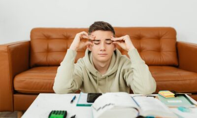 Young man experiencing stress while studying at home, wearing a hoodie.