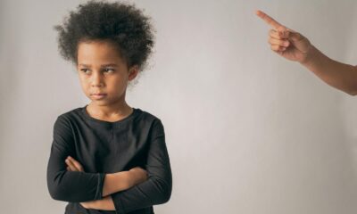 Crop anonymous person pointing up with index finger while scolding unhappy African American girl looking away while standing on white background in studio