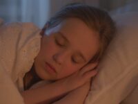 A young girl sleeping peacefully indoors, bathed in warm light.