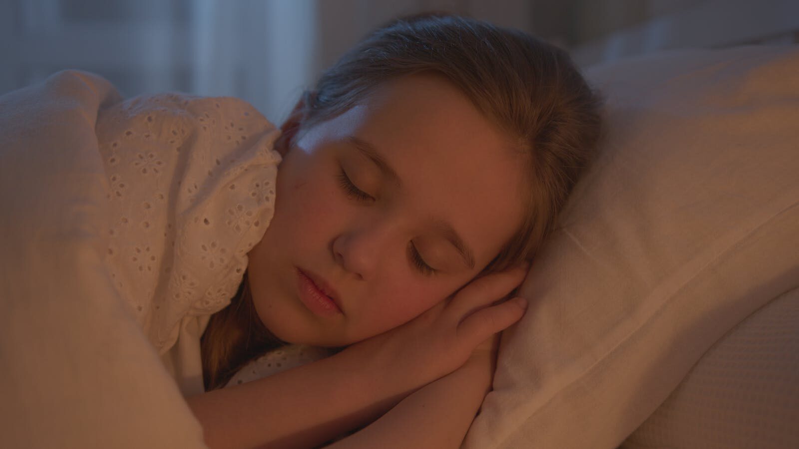 A young girl sleeping peacefully indoors, bathed in warm light.