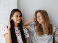 Two happy teen girls smiling together, enjoying a moment indoors. Perfect for friendship and lifestyle themes.
