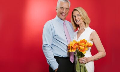 A senior couple poses with tulips against a vibrant red backdrop, exuding joy and love.