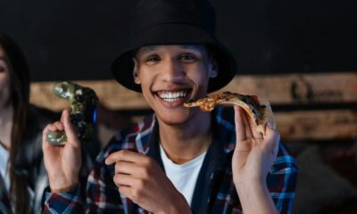 Young man smiling with pizza and joystick indoors, capturing a fun gaming moment.