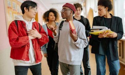 A group of diverse students walking and talking in a school corridor, carrying books and folders.