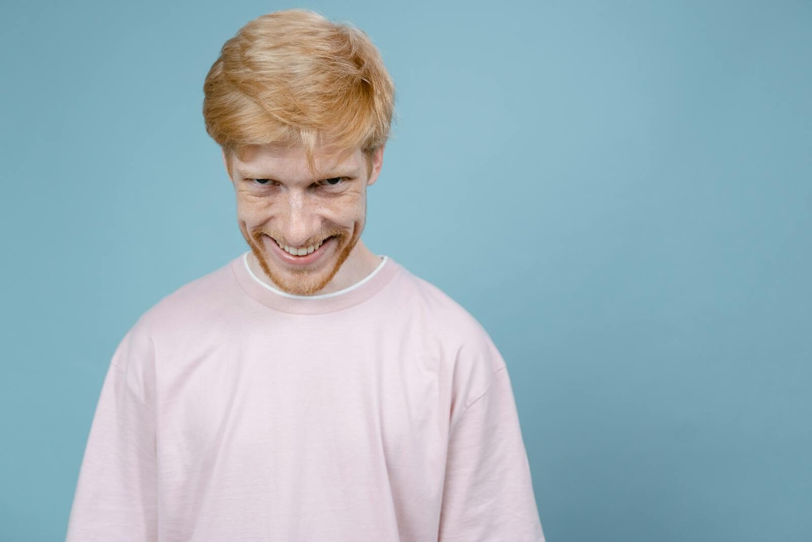 Young man in pink shirt smiles mischievously against blue background in studio setting.