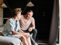 A father bonding with his teenage son in a cozy bedroom, sharing advice and conversation.
